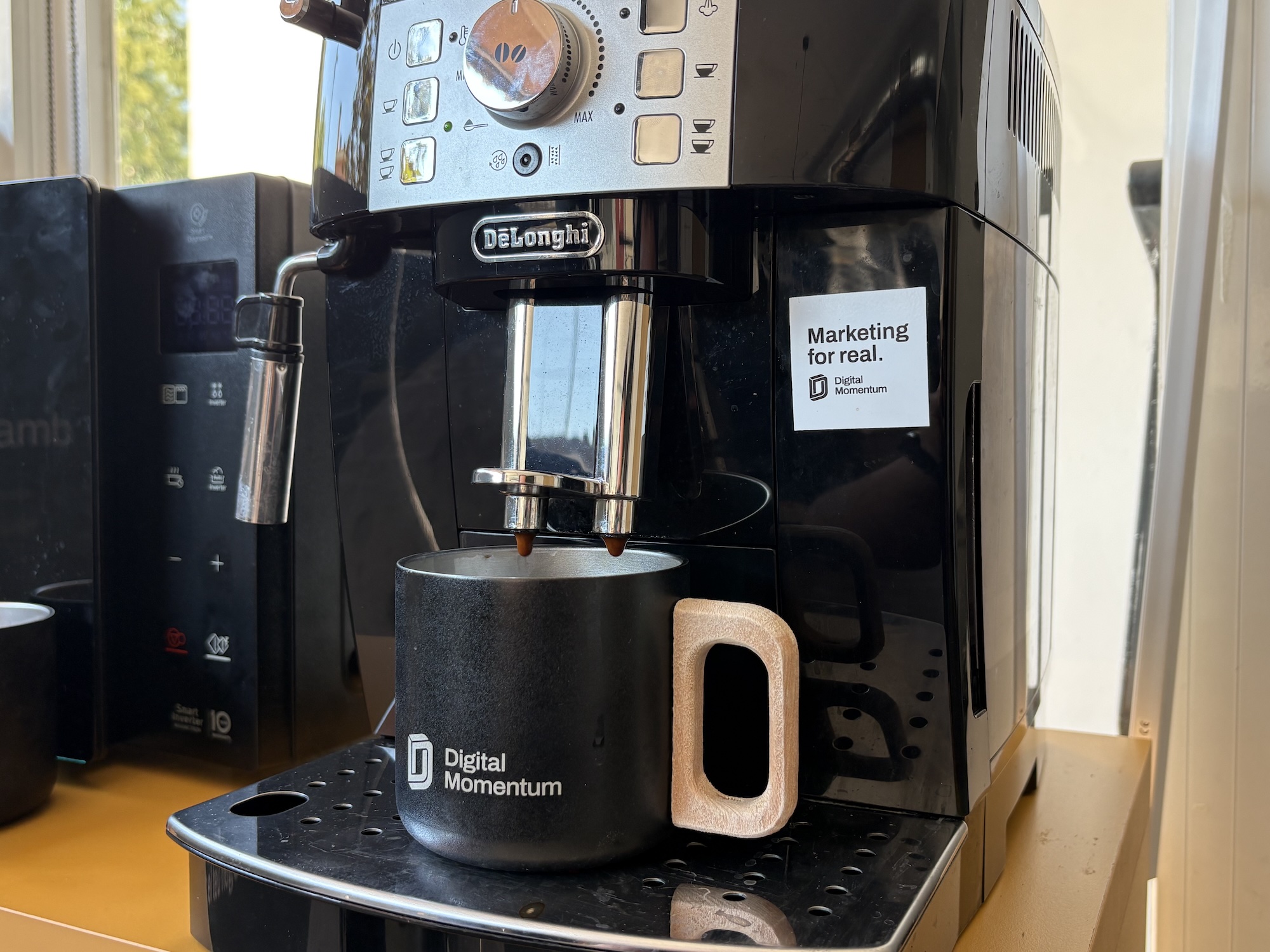 Cafetera preparando un café en una taza metálica con asa de madera con la marca "Digital Momentum"